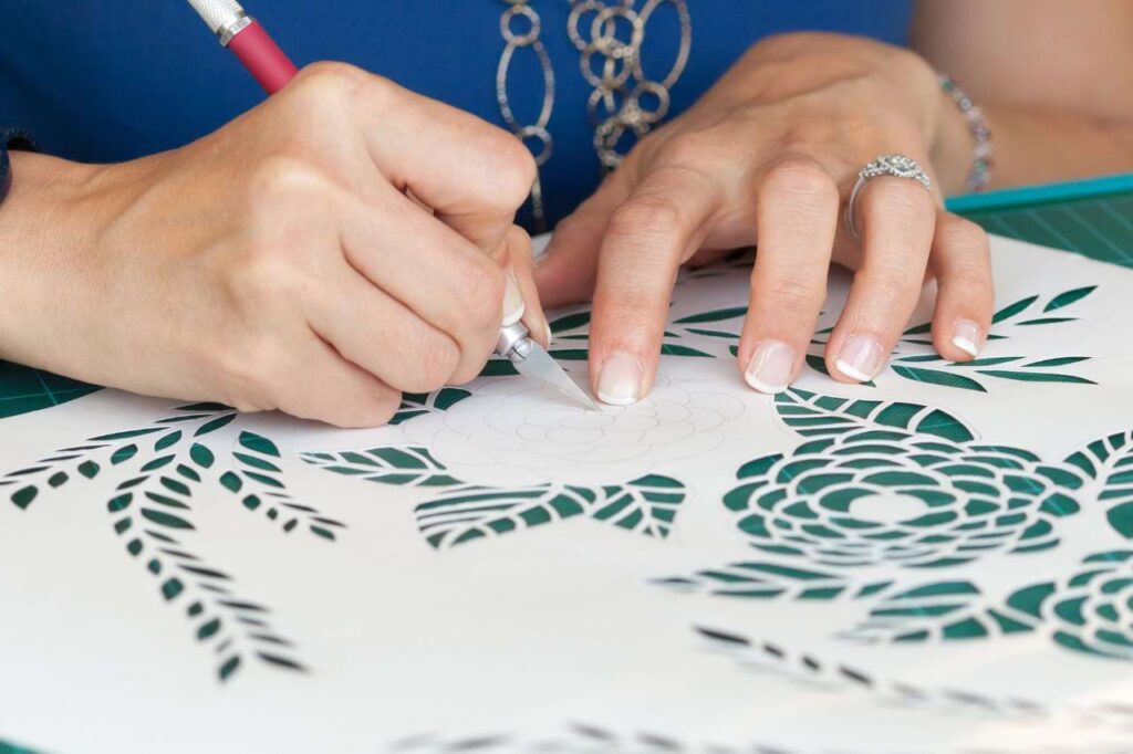 A woman creates a papercut on a cutting board, with an exacto knife